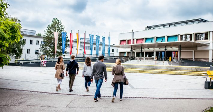 Studierende gehen über den Campus zum Haupteingang der Universität Klagenfurt