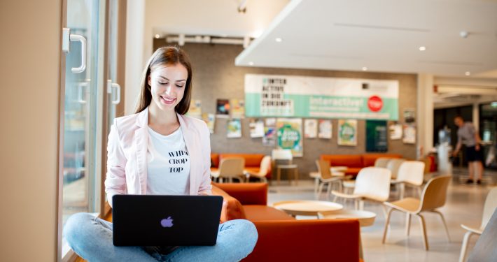 Studentin mit Laptop sitzt am Fenster in der Aula