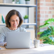 Eine Frau mittleren Alters sitzt lächelnd vor einem Laptop