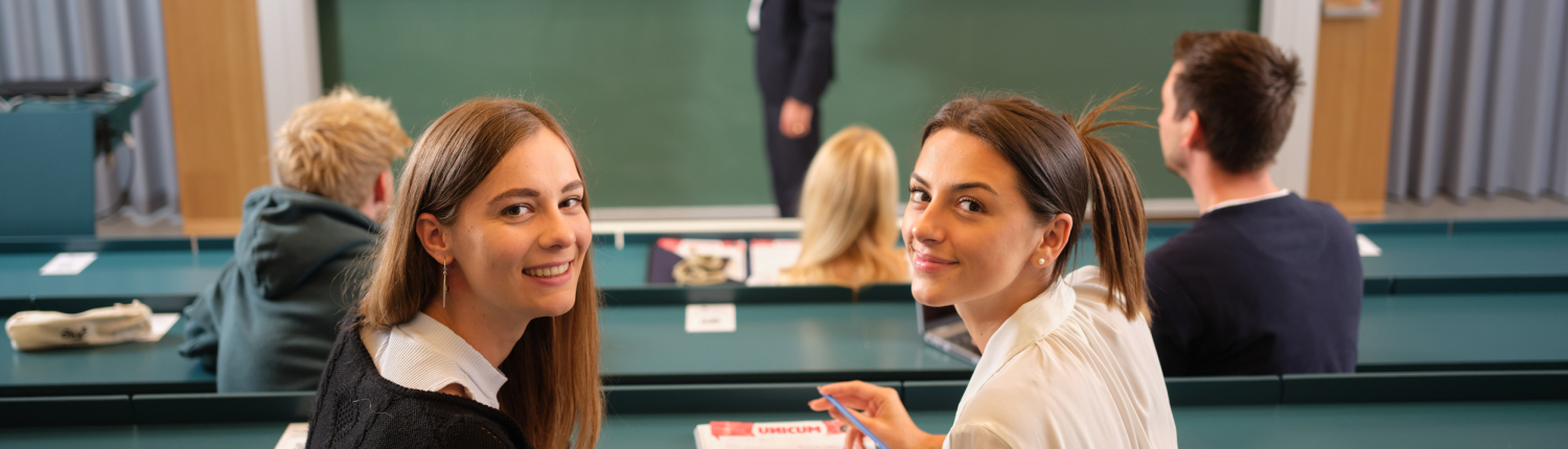 Studierende im Hörsaal schauen in die Kamera