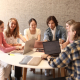 Eine Lerngruppe aus fünf Studierenden sitzt an einem runden Tisch vor der Universitätsbibliothek der Universität Klagenfurt und arbeitet an Laptops.