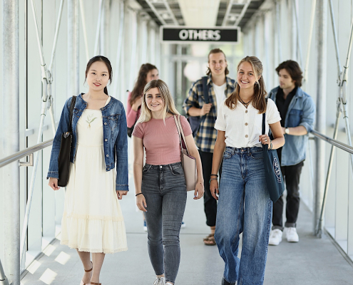 Eine Studierendengruppe geht durch den Verbindungsgang vom Südtrakt in Richtung Zentralgebäude der Universität Klagenfurt.