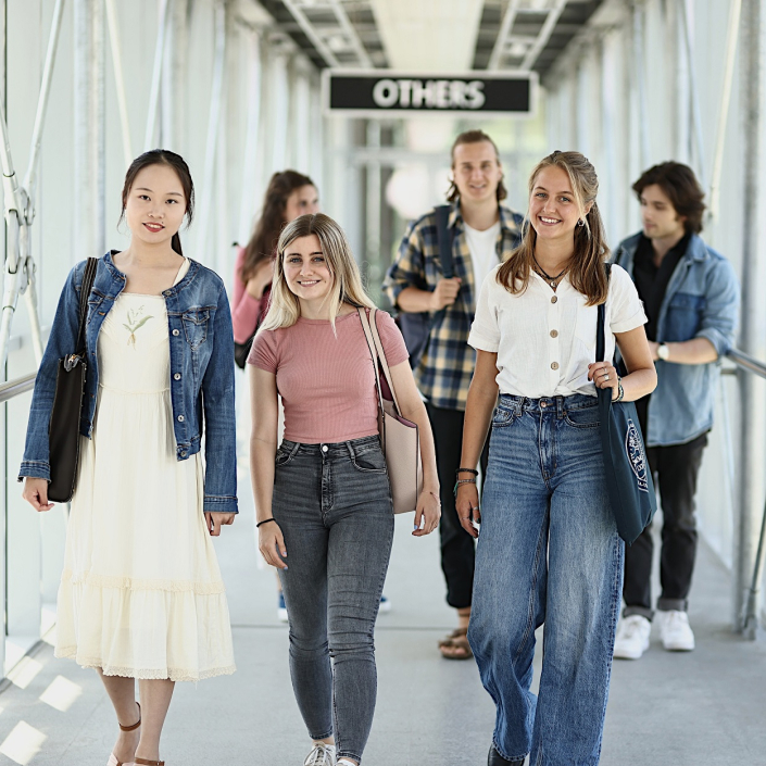 Eine Studierendengruppe geht durch den Verbindungsgang vom Südtrakt in Richtung Zentralgebäude der Universität Klagenfurt.