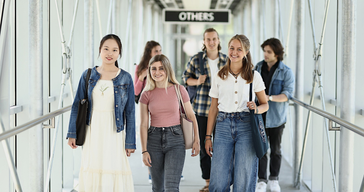 Eine Studierendengruppe geht durch den Verbindungsgang vom Südtrakt in Richtung Zentralgebäude der Universität Klagenfurt.