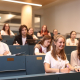 Mehrere Studierende sitzen in den gestuften blaufarbigen Sitzreihen eines Hörsaals der Universität Klagenfurt.