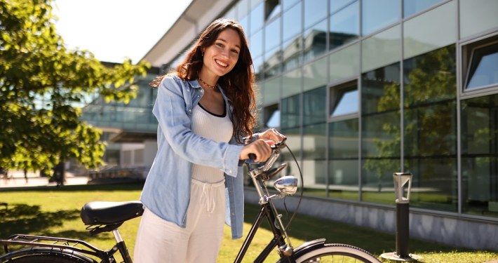 Studierende der Universität Klagenfurt steht mit einem schwarzen Fahrrad vor einem Gebäude auf dem Campus.