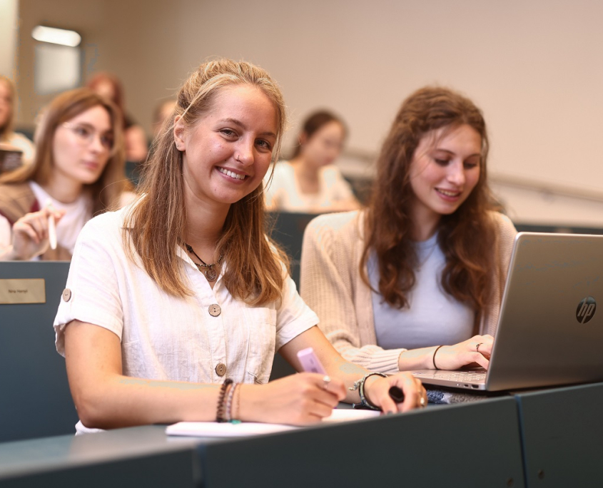 Mehrere Studierende sitzen in den gestuften blaufarbigen Sitzreihen eines Hörsaals der Universität Klagenfurt.