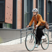 Radfahrerin mit weißem Fahrradhelm in orangefarbenem Blazer vor Gebäude.